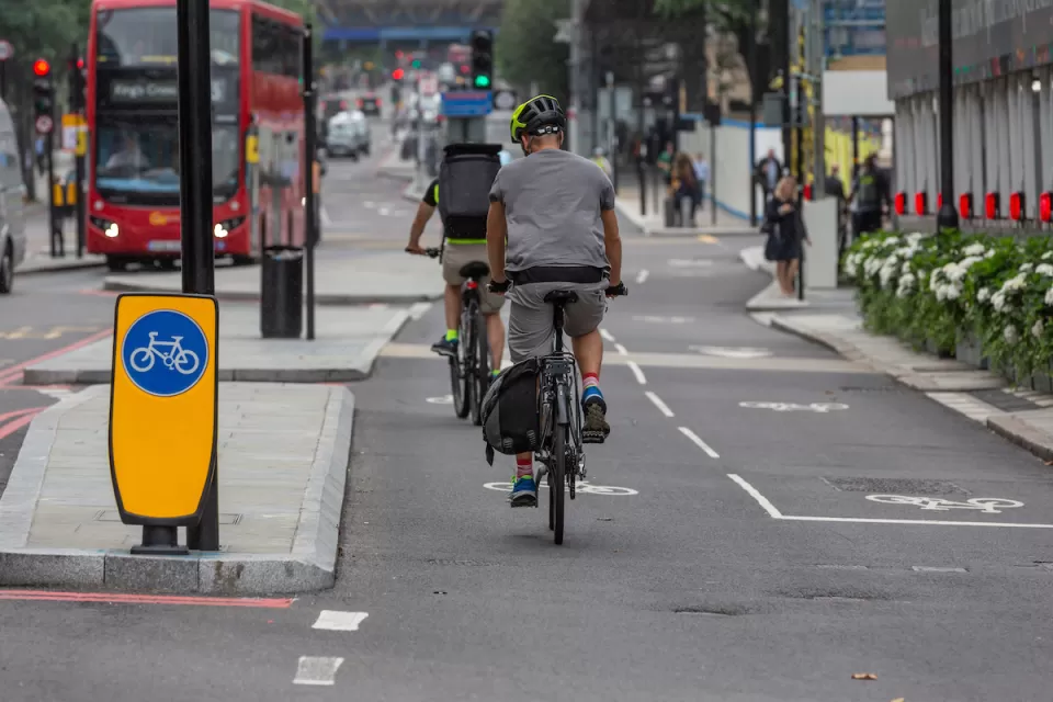 Protected two-way cycletrack on street in London, UK with red double-decker bus in background.